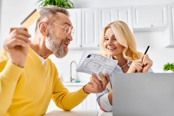 A mature loving couple in cozy homewear examining a piece of paper together in their kitchen at home. — Stock Photo