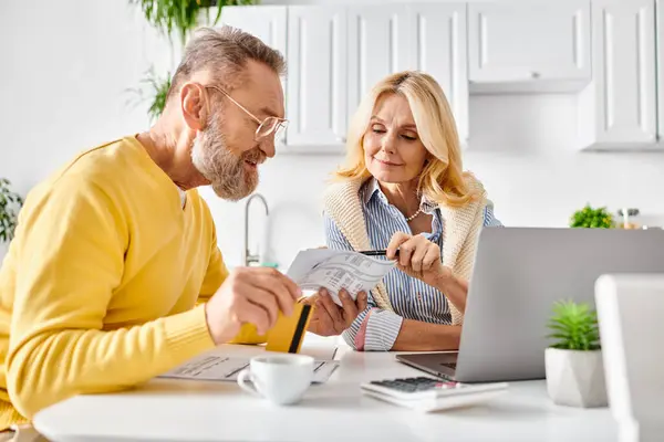 A mature man and woman reading a piece of paper together in their cozy kitchen at home. — Stock Photo