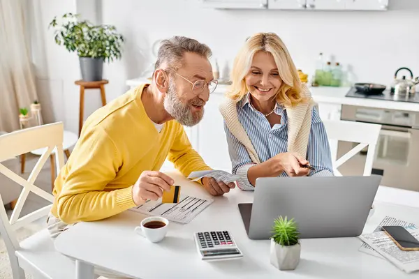 A mature couple in cozy homewear sit at a table, engrossed in using a laptop and calculator for joint projects. — Stock Photo