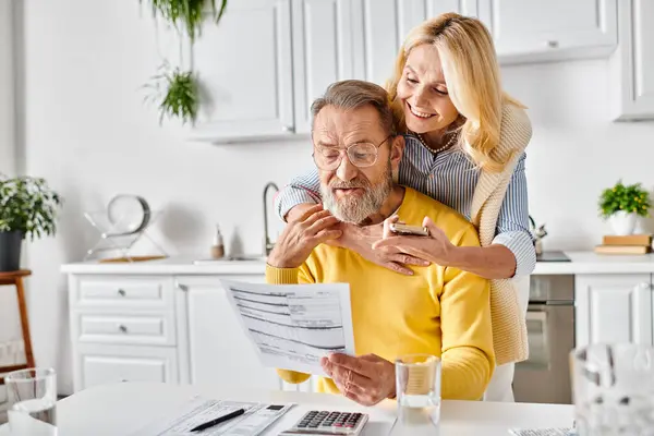 A mature loving couple in cozy homewear examining a mysterious piece of paper in their kitchen at home. — Stock Photo