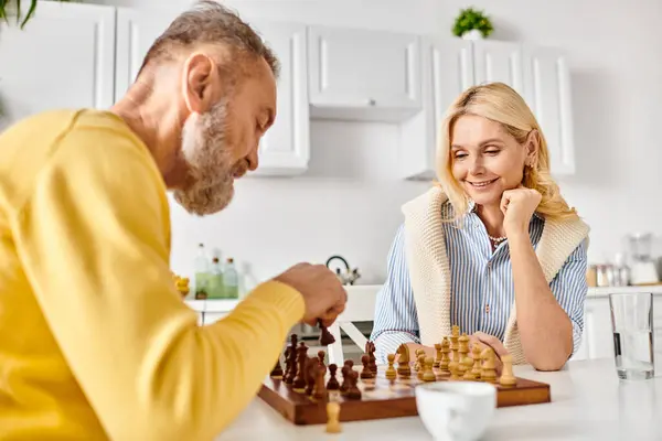 A mature loving couple in cozy homewear engage in a strategic game of chess, focused and immersed in the competition. — Stock Photo