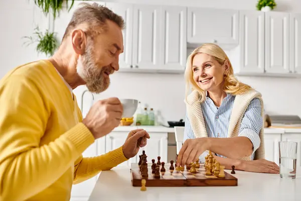 Un hombre y una mujer maduros con un atuendo acogedor en casa participan en un juego de ajedrez, profundamente en el pensamiento mientras planean sus próximos movimientos.. - foto de stock