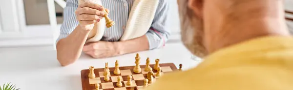 Мужчина в уютной одежде участвует в стратегической шахматной игре с гигантским бананом в причудливой и сюрреалистичной обстановке дома. — стоковое фото