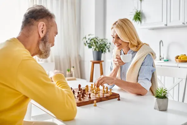 Зрелая любящая пара в уютном домашнем платье, участвующая в интенсивной игре в шахматы, вырабатывающая стратегию и делающая расчетливые ходы. — стоковое фото