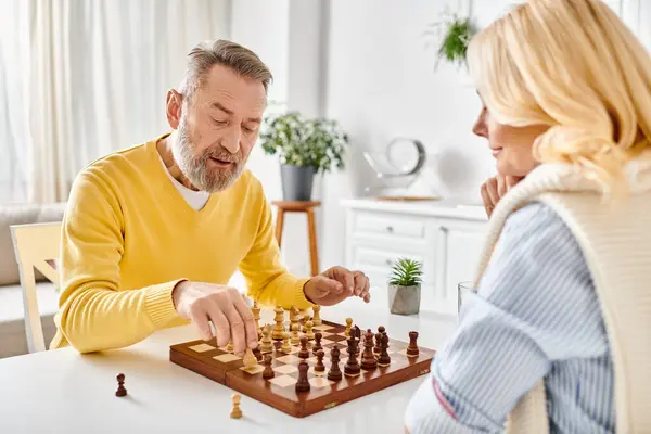 Um casal maduro e amoroso em roupa de casa aconchegante envolvido em um jogo competitivo de xadrez, focado no tabuleiro diante deles. — Fotografia de Stock