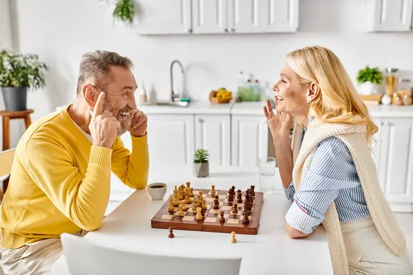 A man and woman in cozy homewear sit at a table engaged in a game of chess, focusing intently on their moves. — Stock Photo