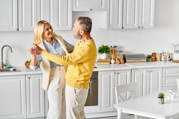 Зріла любляча пара в затишному домашньому вбранні танцює витончено на своїй кухні, насолоджуючись компанією один одного. — стокове фото