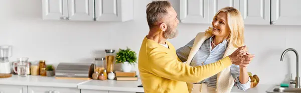 A mature man holds a woman lovingly in a cozy kitchen setting at home. — Stock Photo
