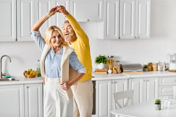 Un couple aimant mature dans des vêtements confortables se tiennent ensemble dans leur cuisine, partageant un moment de convivialité. — Photo de stock