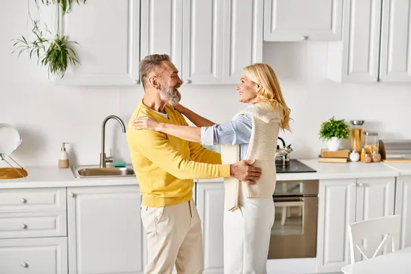 Ein reifes, liebevolles Paar in kuscheliger Hauskleidung, das zu Hause Zeit miteinander in der Küche verbringt. — Stockfoto