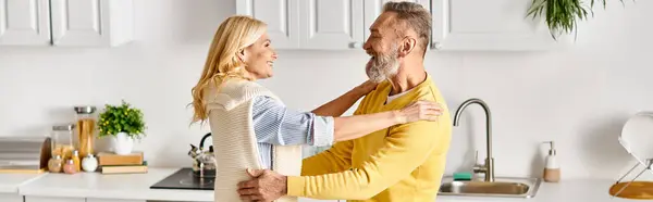 Ein reifer Mann umarmt Frau in einer liebevollen Umarmung in ihrer gemütlichen Küche zu Hause. — Stockfoto