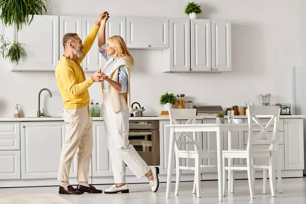 A mature loving couple in cozy homewear dancing joyfully in their kitchen together at home. — Stock Photo