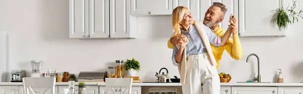 Una pareja amorosa madura en ropa de casa acogedora de pie juntos en una cocina caliente, compartiendo un momento de unión y conexión. - foto de stock