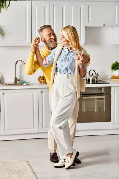 A mature loving couple in cozy homewear joyfully dancing in their kitchen, connecting through movement and music. — Stock Photo