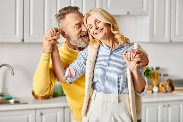 Una pareja madura y cariñosa vestida con acogedora ropa de casa bailando alegremente en su cocina en casa. — Stock Photo