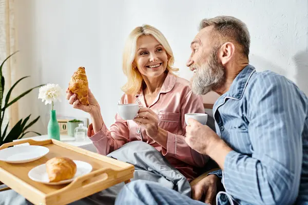 A mature loving couple in casual homewear enjoying a meal together at a table in their bedroom. — Stock Photo