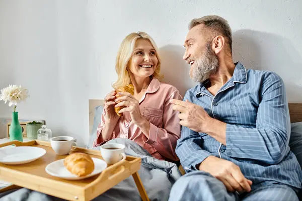 A mature loving couple relaxes on a couch, enjoying a meal together in their bedroom. — Stock Photo