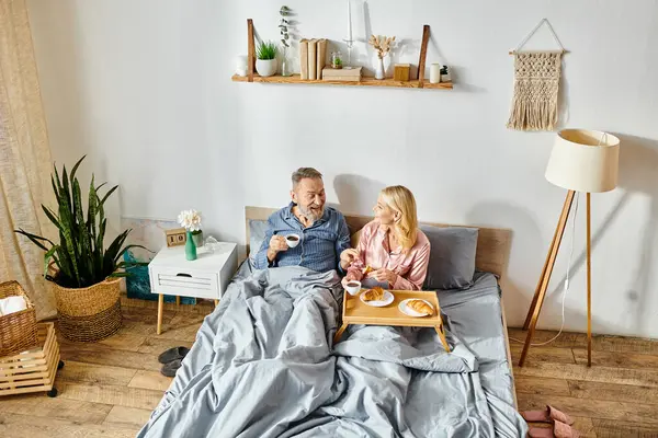 Um casal amável maduro em roupa de casa aconchegante sentar juntos em uma cama, desfrutando de um momento pacífico de união. — Fotografia de Stock