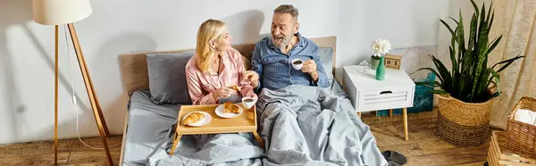 Una coppia matura e amorevole, vestita con abiti da casa accoglienti, si siede a stretto contatto su un letto, condividendo un momento di tenerezza e connessione.. — Foto stock