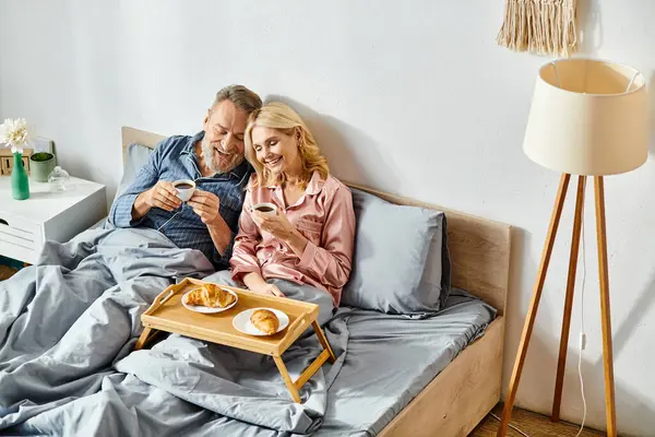 Mature loving couple in cozy homewear sitting on bed, enjoying each other — Stock Photo