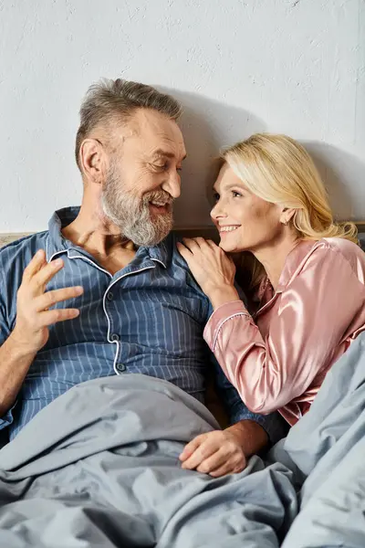 A mature loving couple, dressed in cozy homewear, peacefully laying together in bed, enjoying each others company. — Stock Photo