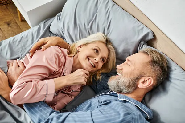 Un couple aimant mature dans des vêtements confortables couchés ensemble sur un lit, partageant un moment paisible d'intimité et de connexion. — Photo de stock