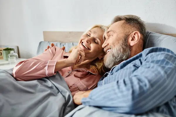 Ein reifer Mann und eine reife Frau in kuscheliger Hauskleidung liegen zusammen im Bett und teilen einen friedlichen Moment der Intimität und Verbundenheit. — Stockfoto