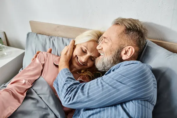 A mature loving couple in cozy homewear lying together in bed, sharing a quiet and intimate moment. — Stock Photo