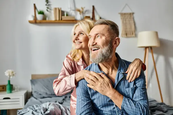 A mature man and woman sit comfortably on a bed in cozy homewear, enjoying each others company. — Stock Photo