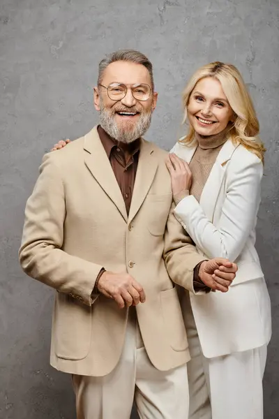 Um homem e uma mulher ao lado um do outro, exalando elegância em trajes debonair em um pano de fundo cinza. — Fotografia de Stock