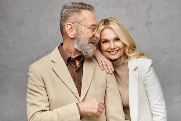 Un homme et une femme mûrs en tenue élégante se tiennent étroitement ensemble, exsudant élégance et affection sur un fond gris. — Photo de stock