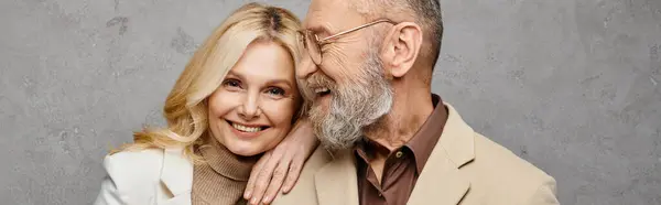 Зріла, елегантна пара в одязі deonair позує витончено на сірому тлі. — стокове фото