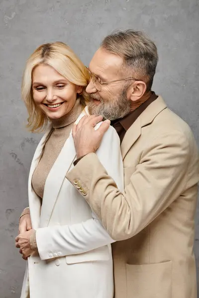 Un hombre y una mujer elegantes y maduros se unen en trajes elegantes sobre un fondo gris. - foto de stock