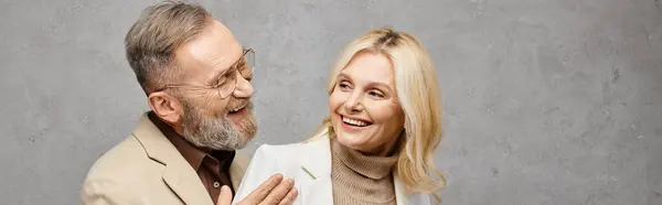 A mature man and woman stand stylishly next to each other in elegant attire on a gray backdrop. — Stock Photo