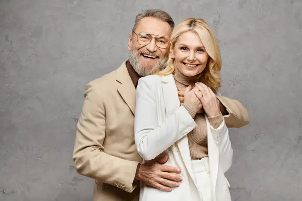 A mature man and woman, exuding elegance, pose together in stylish attire against a gray backdrop. — Stock Photo
