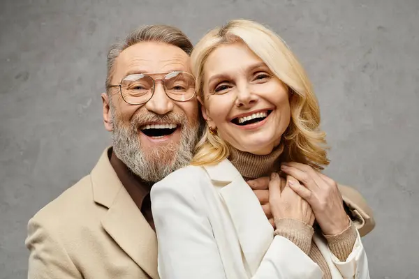 Un homme et une femme mûrs élégamment habillés, souriant joyeusement devant un fond gris. — Photo de stock