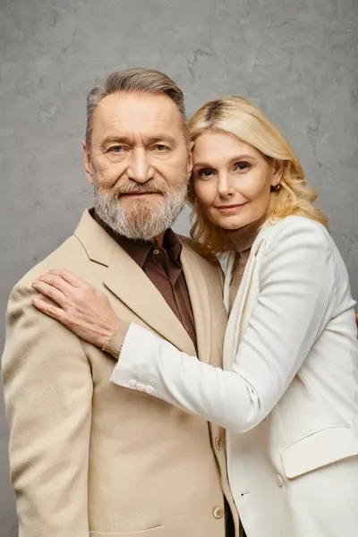 Mature couple dressed elegantly pose together in front of a gray backdrop. — Stock Photo