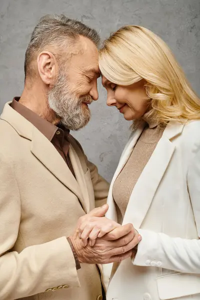 Una pareja madura y cariñosa en atuendo debonair tomados de la mano y sonriendo sobre un fondo gris. - foto de stock