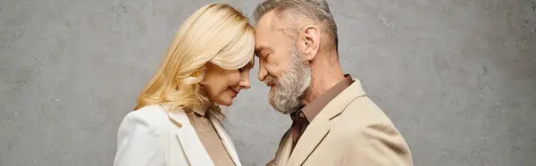 An elegant, mature man and woman in debonair attire stand together against a gray backdrop. — Stock Photo