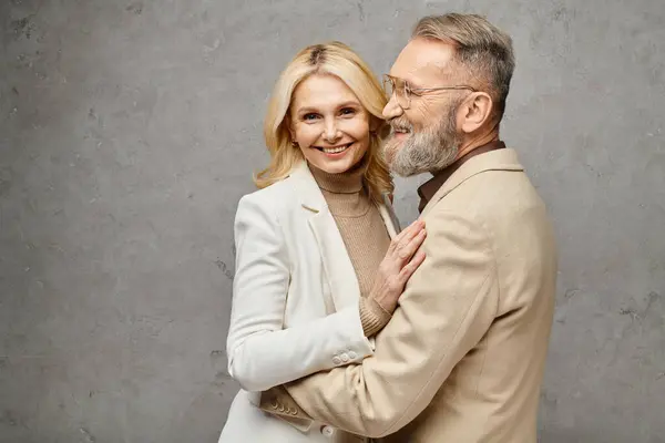 A mature man and woman in elegant attire embrace each other tenderly against a gray backdrop. — Stock Photo