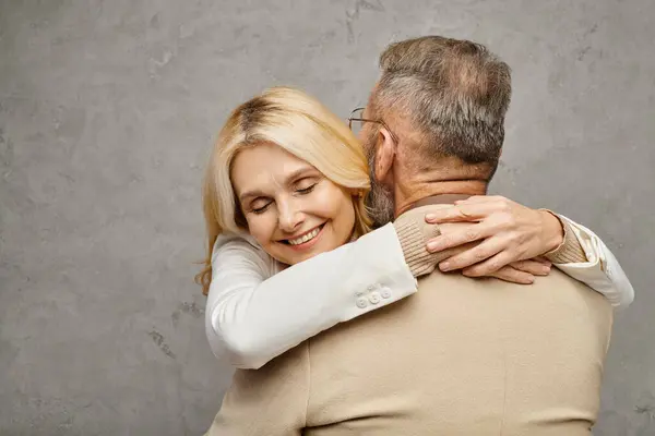 A mature man and woman, elegantly dressed, embracing each other tenderly against a gray backdrop. — Stock Photo