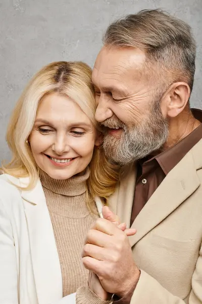 A mature man and woman, dressed elegantly, share a tender hug on a gray backdrop. — Stock Photo