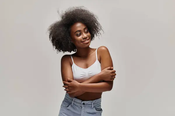 Uma jovem mulher afro-americana elegante orgulhosamente se levanta com os braços cruzados, mostrando seu afro deslumbrante. — Fotografia de Stock