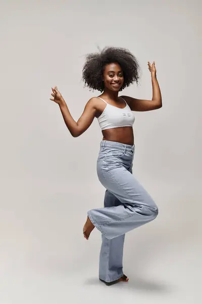 A young African American woman with curly hair dances gracefully in a white top in a studio setting. — Stock Photo