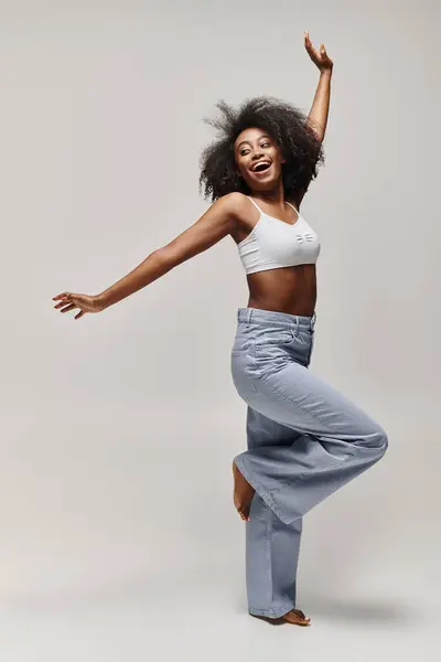 A beautiful young African American woman with curly hair dances energetically in a white top in a studio setting. — Stock Photo