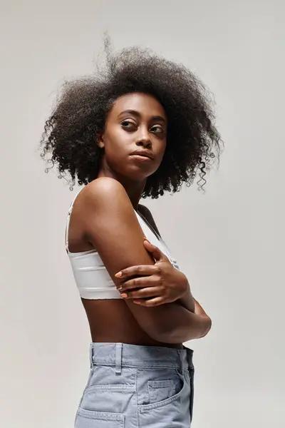 Fiduciosa donna afro-americana con capelli ricci in piedi con le braccia incrociate, trasudando forza e responsabilizzazione. — Foto stock