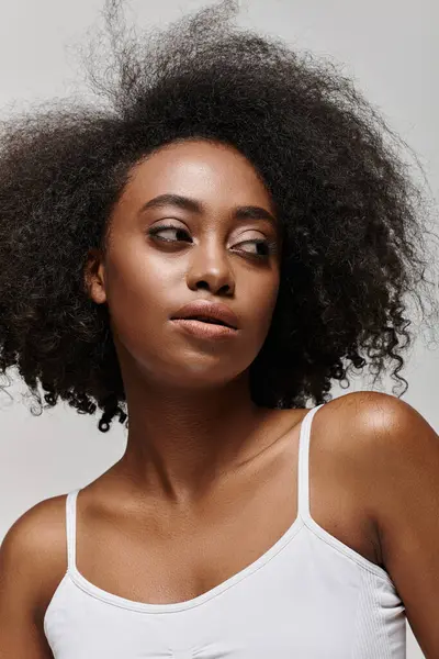 Una hermosa mujer afroamericana con el pelo rizado da una pose en un ambiente de estudio. - foto de stock