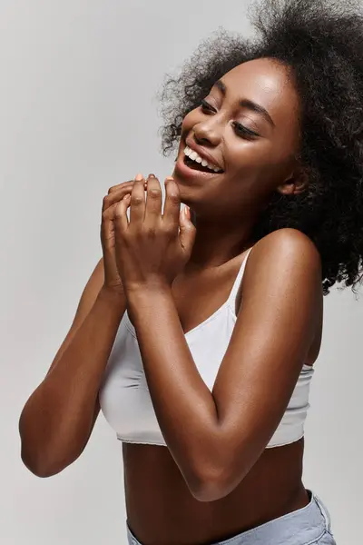 Uma bela jovem afro-americana com cabelo encaracolado vestindo um top branco, sorrindo brilhantemente e batendo palmas. — Fotografia de Stock