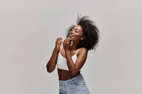 A stunning African American woman with curly hair poses elegantly in a white top and denim skirt, exuding grace and style. — Stock Photo