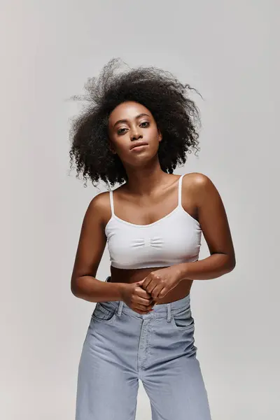 Eine schöne junge Afroamerikanerin mit lockigem Haar posiert in weißem Top und Jeans. — Stockfoto